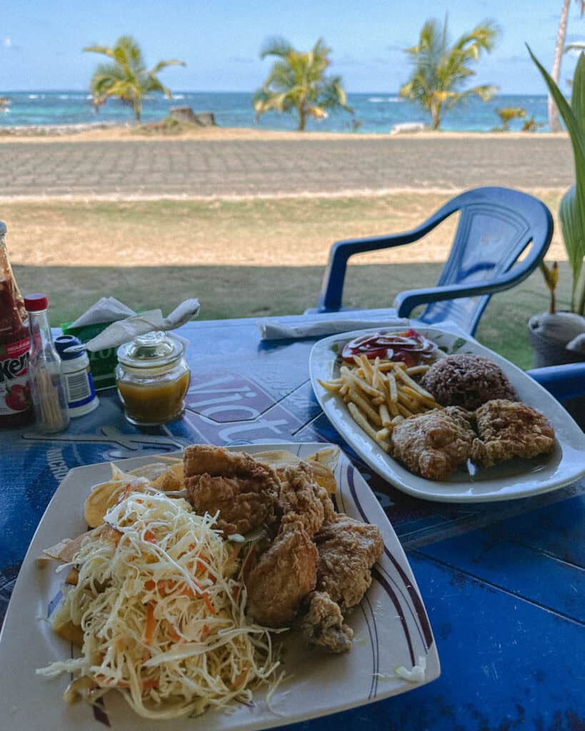 Corn Islands Nicaragua: Paradise on Big & Little Corn 32 Two plates of fried chicken meals on a table at Bar Victorias on Big Corn Island, set against a backdrop of the sea and palm trees.