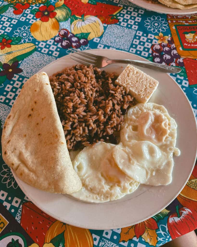 Big Corn Island, Nicaragua: The Underrated Corn Island 45 A traditional Nicaraguan breakfast plate featuring fried eggs, rice and beans, a slice of fresh cheese, and a tortilla, served on a colorful tablecloth at Comedor Doña Julia.