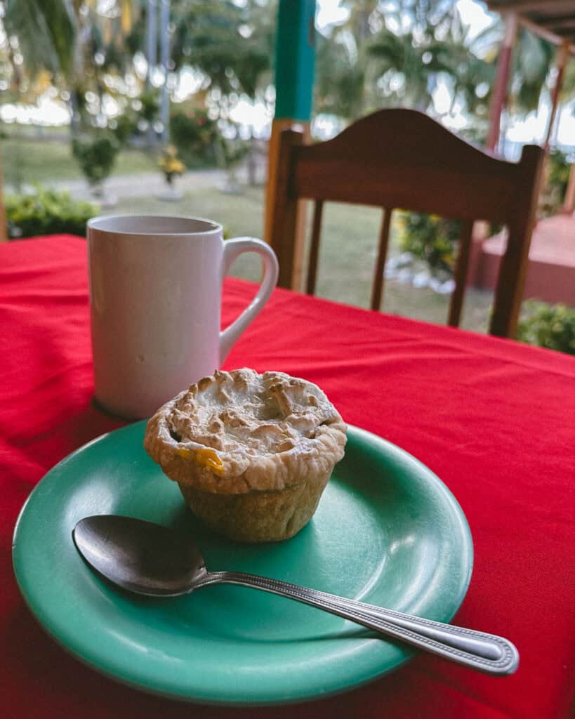 Big Corn Island, Nicaragua: The Underrated Corn Island 41 A close-up of a muffin and a cup of coffee on a red tablecloth at Island Bakery and Sweets on Big Corn Island, with a garden view in the background.