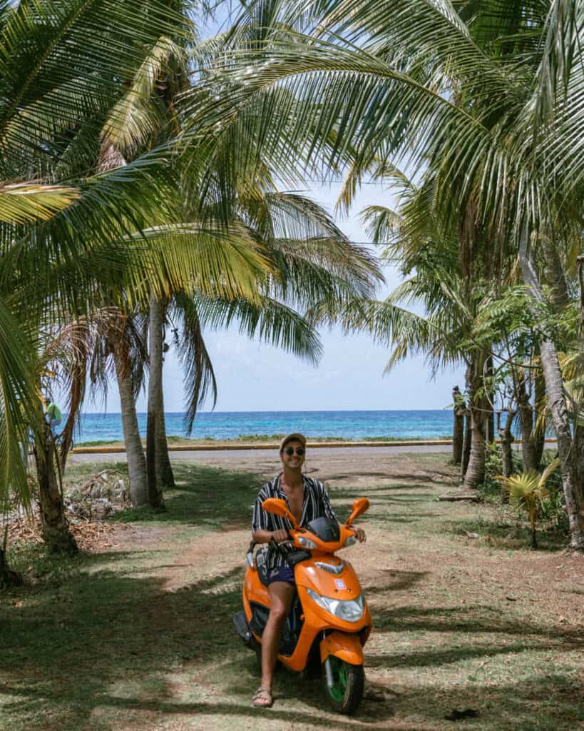 Big Corn Island, Nicaragua: The Underrated Corn Island 13 Brayden on an orange scooter, parked among palm trees near the shore on Big Corn Island.