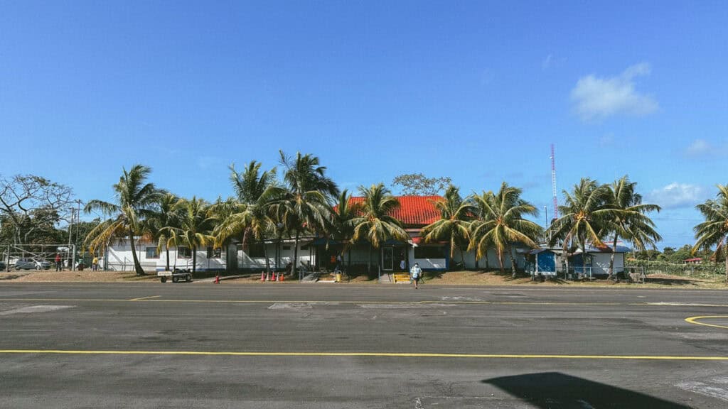 Corn Islands Nicaragua: Paradise on Big & Little Corn 47 The tiny airport on Big Corn Island, Nicaragua, featuring a modest building with a red roof surrounded by tall palm trees under a sunny sky.