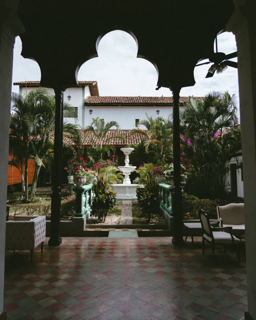 Granada, Nicaragua Travel Guide: Our Honest Thoughts 13 Interior courtyard of Hotel Dario in Granada, Nicaragua, featuring a tiled floor, an ornate fountain, and lush tropical plants with vibrant bougainvillea.