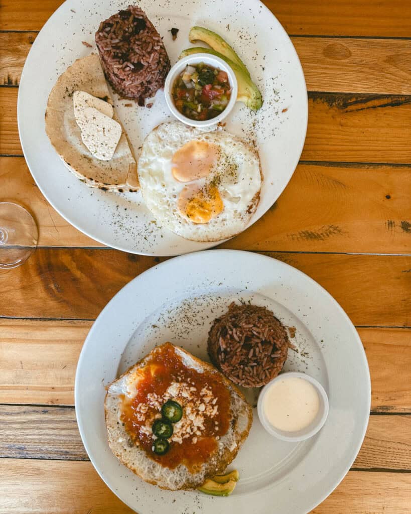 Granada, Nicaragua Travel Guide: Our Honest Thoughts 24 A traditional Nicaraguan breakfast with gallo pinto, fried eggs, tortilla, and avocado slices, presented on white plates over a rustic table at La Sultana y El Cafe.