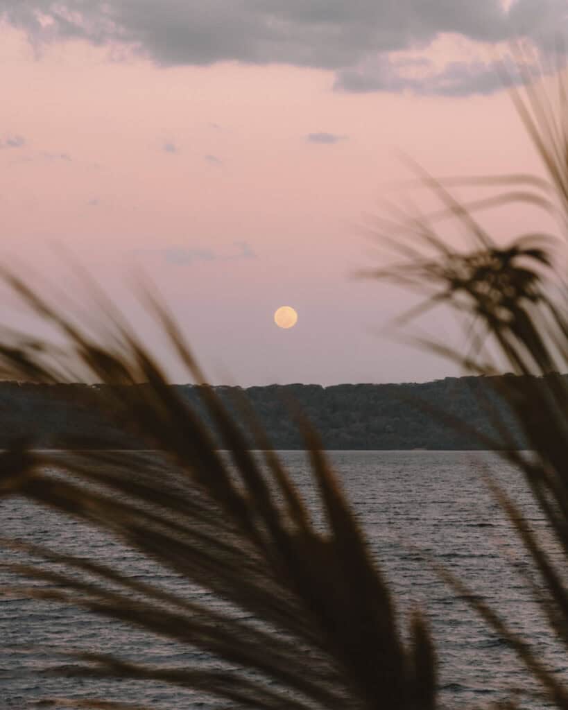 Laguna de Apoyo, Nicaragua Travel Guide (Stay > Day) 14 The full moon rising over Laguna de Apoyo, viewed through silhouetted palm fronds under a pastel-colored sky.