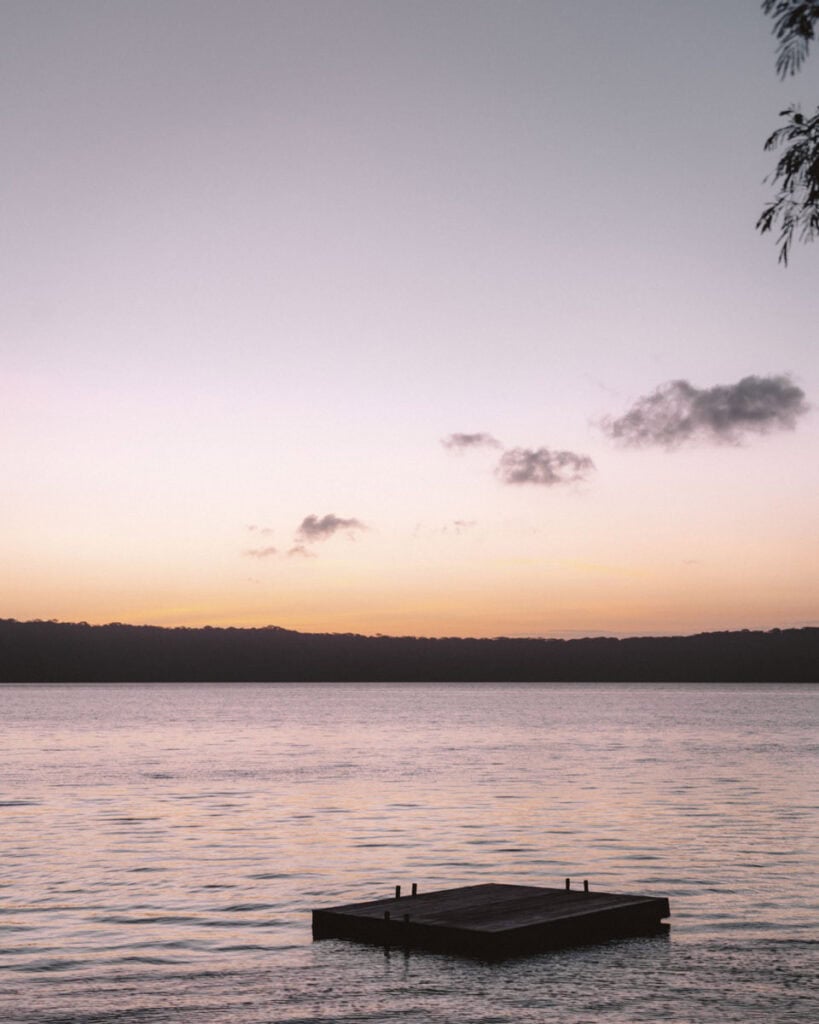 Laguna de Apoyo, Nicaragua Travel Guide (Stay > Day) 12 A serene view of a pontoon on Laguna de Apoyo at sunrise, with soft pastel hues reflecting on the calm water.