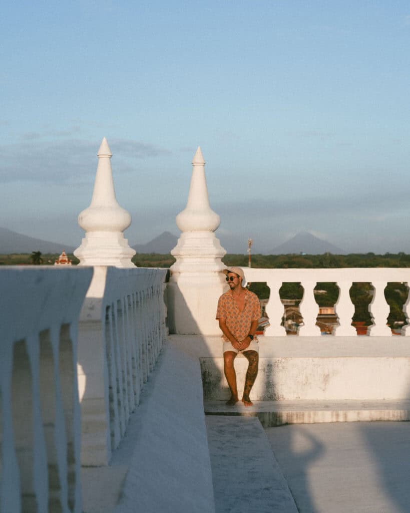 18 Best Things to Do in Leon, Nicaragua 14 Brayden seated on the rooftop of León Cathedral, wearing a patterned shirt, with distant volcanoes and countryside visible in the background.