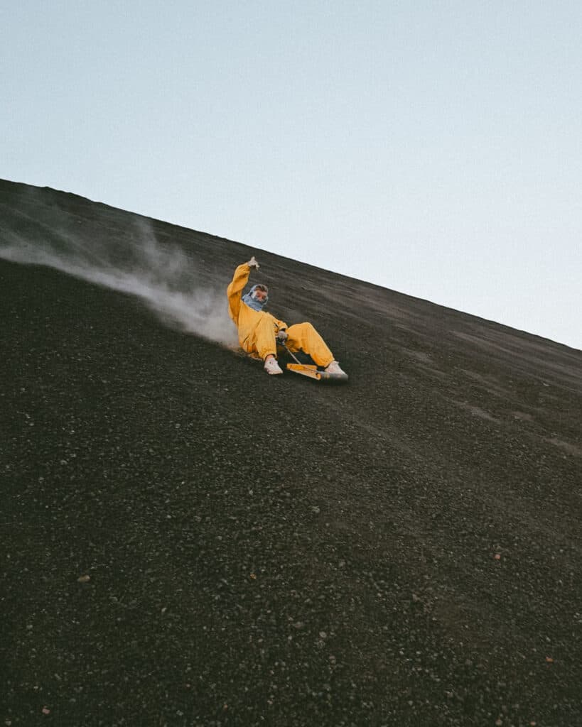 Epic Volcano Boarding in Nicaragua at Cerro Negro Volcano 21 Sally sliding down the steep slope of Cerro Negro, wearing a yellow suit and helmet, with a dramatic volcanic landscape surrounding her.