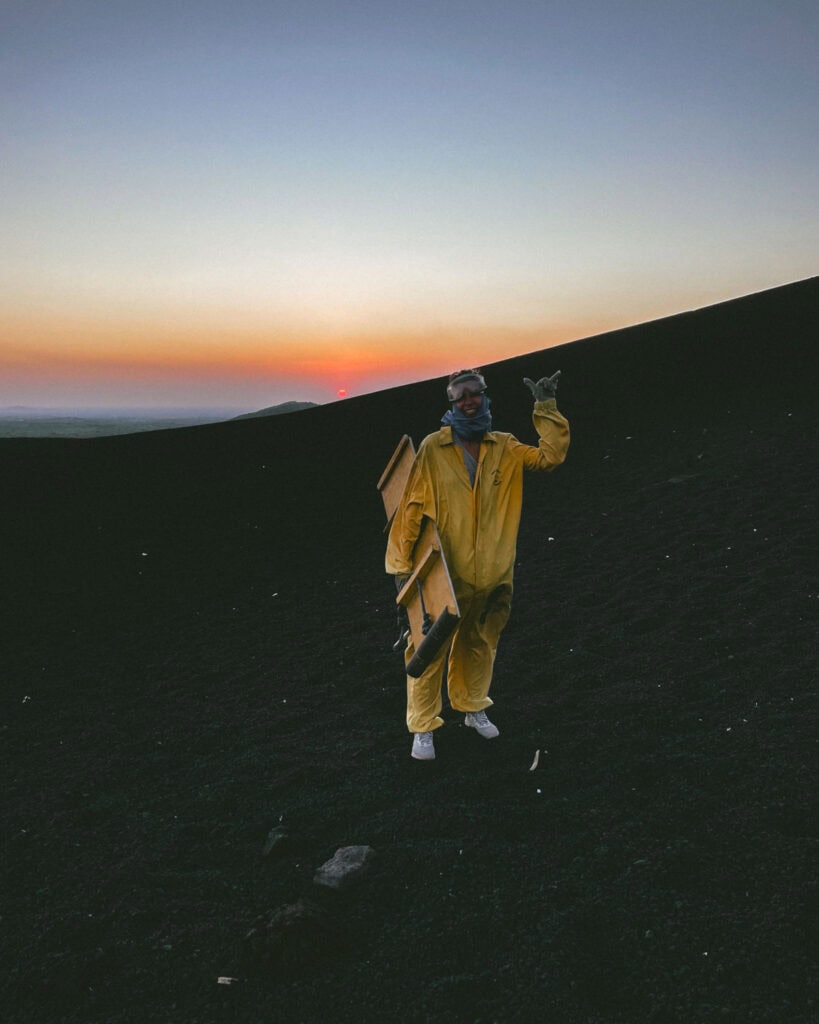 Epic Volcano Boarding in Nicaragua at Cerro Negro Volcano 22 Sally standing at the base of Cerro Negro Volcano in her yellow volcano boarding overalls and goggles with a sunset behind her.
