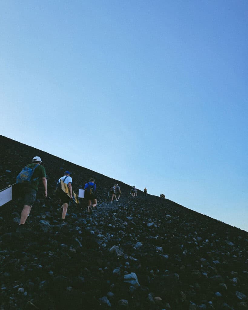 Epic Volcano Boarding in Nicaragua at Cerro Negro Volcano 3 A trail of tourists climbing the black, rocky slopes of the Cerro Negro Volcano with volcano boards in hand.