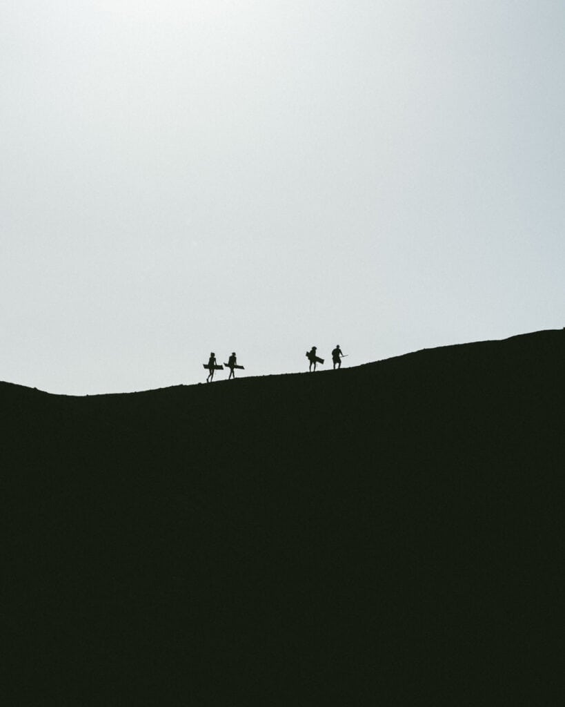 Epic Volcano Boarding in Nicaragua at Cerro Negro Volcano 16 A silhouette of four tourists climbing the black slopes of Cerro Negro Volcano against a golden sun.