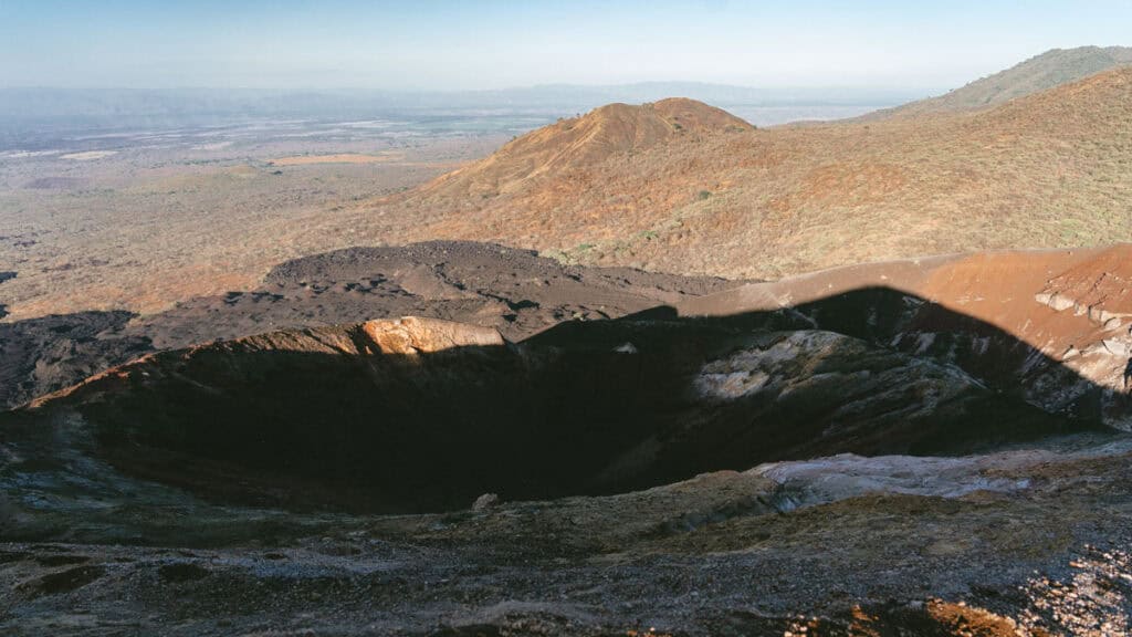 Epic Volcano Boarding in Nicaragua at Cerro Negro Volcano 17 The rugged, volcanic crater of Cerro Negro under clear skies, surrounded by ash-covered slopes and green vegetation in the distance.