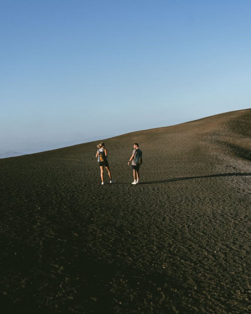 18 Best Things to Do in Leon, Nicaragua 41 Sally and Brayden walking together across the black sands of Cerro Negro, Nicaragua, their shadows elongated in the late afternoon sun.