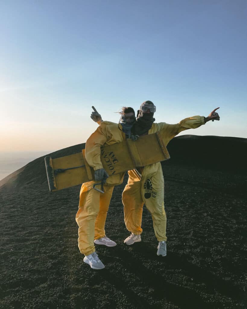 Epic Volcano Boarding in Nicaragua at Cerro Negro Volcano 18 A close-up shot of Sally and Brayden in yellow protective suits and goggles, ready for volcano boarding on Cerro Negro, with the dark volcanic slope behind them.