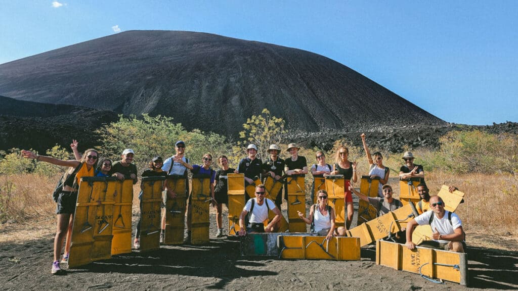Epic Volcano Boarding in Nicaragua at Cerro Negro Volcano 15 A tour group dressed in yellow jumpsuits poses with their wooden boards in front of Cerro Negro's towering volcanic cone in Leon, Nicaragua.