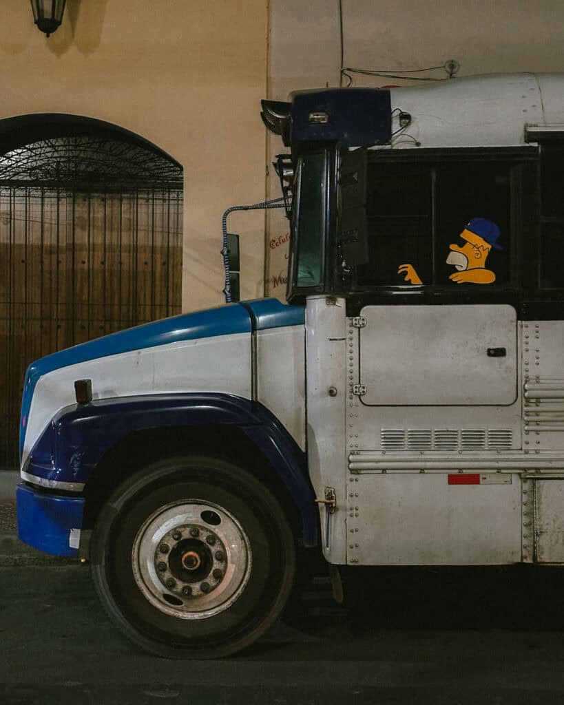 Nicaragua Travel Guide: Land of Lakes and Volcanoes 42 A colorful chicken bus parked on a street in Leon, Nicaragua, with a playful cartoon of Homer Simpson driving painted on its side.