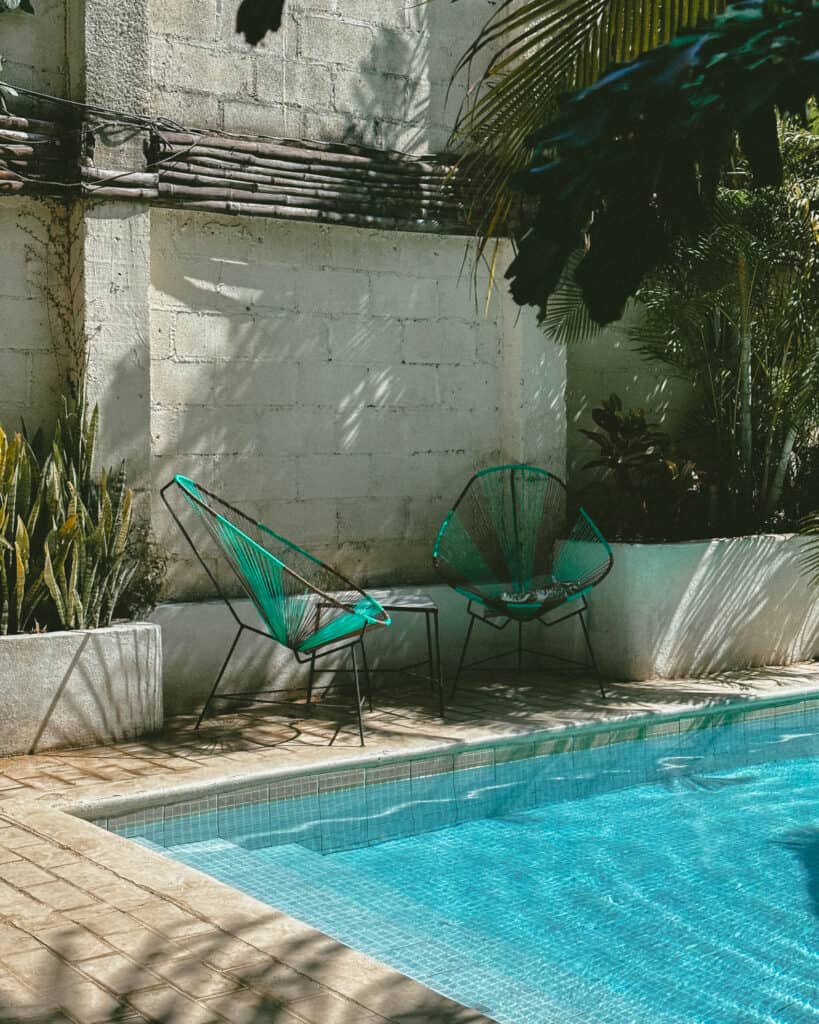 18 Best Things to Do in Leon, Nicaragua 31 A serene poolside in Coco Calala, Leon, featuring two green lounge chairs under palm trees, next to a glimmering blue pool.