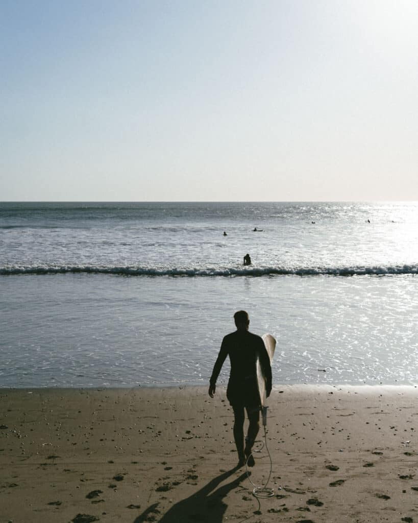 18 Best Things to Do in Leon, Nicaragua 50 Brayden walks towards the waves at Las Peñitas beach in Nicaragua, carrying a surfboard, with the sun glistening over the water during the golden hour.