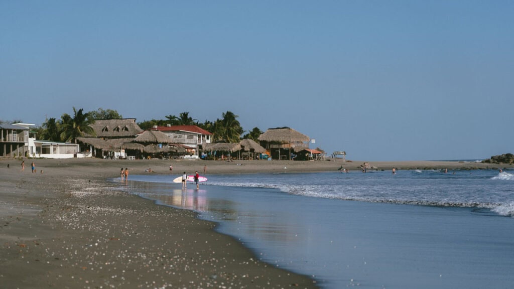 Epic Volcano Boarding in Nicaragua at Cerro Negro Volcano 10 A wide view of Las Peñitas Beach in León, Nicaragua, showing thatched-roof huts and a few people enjoying the shoreline.