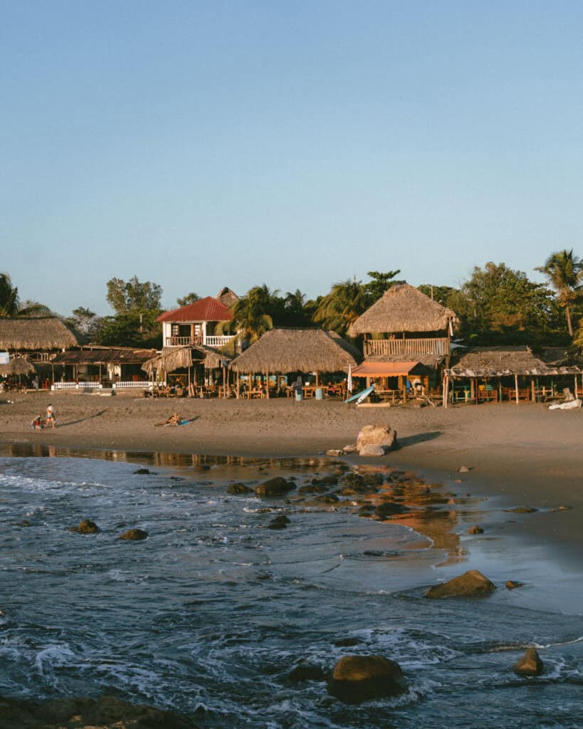 Hiking Telica Volcano in Nicaragua: A Magical Sunrise 18 A close-up perspective of Las Peñitas Beach with rustic huts and calm waves along the rocky shoreline, bathed in a warm, golden light at sunset.