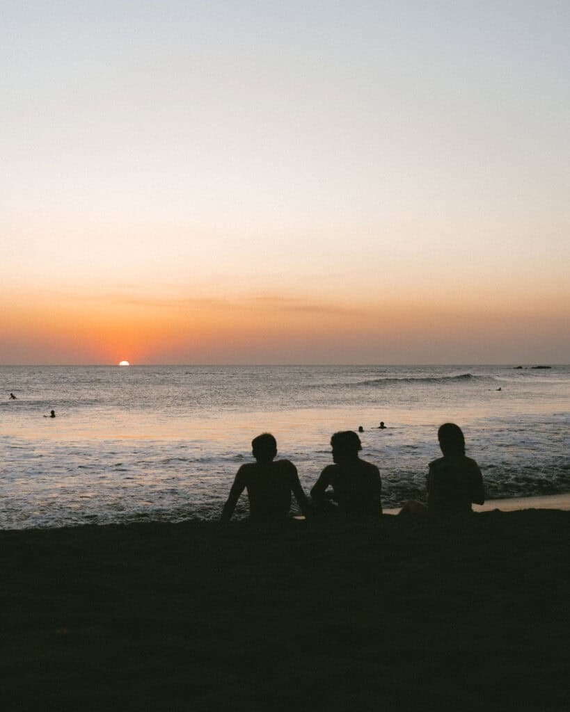18 Best Things to Do in Leon, Nicaragua 52 Silhouetted figures of three friends sitting on the sand as the sun sets over Las Peñitas Beach in Leon, Nicaragua.