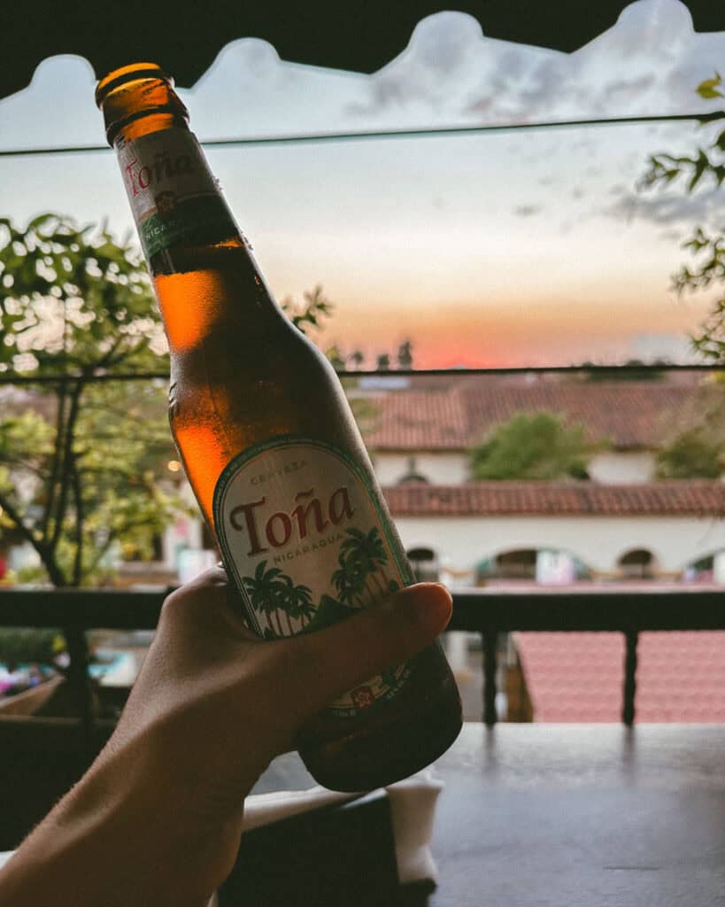 Leon, Nicaragua Travel Guide: The City of Revolution 33 A scenic view from El Mirador bar in León, Nicaragua, with a Toña beer held up against the backdrop of a glowing sunset.
