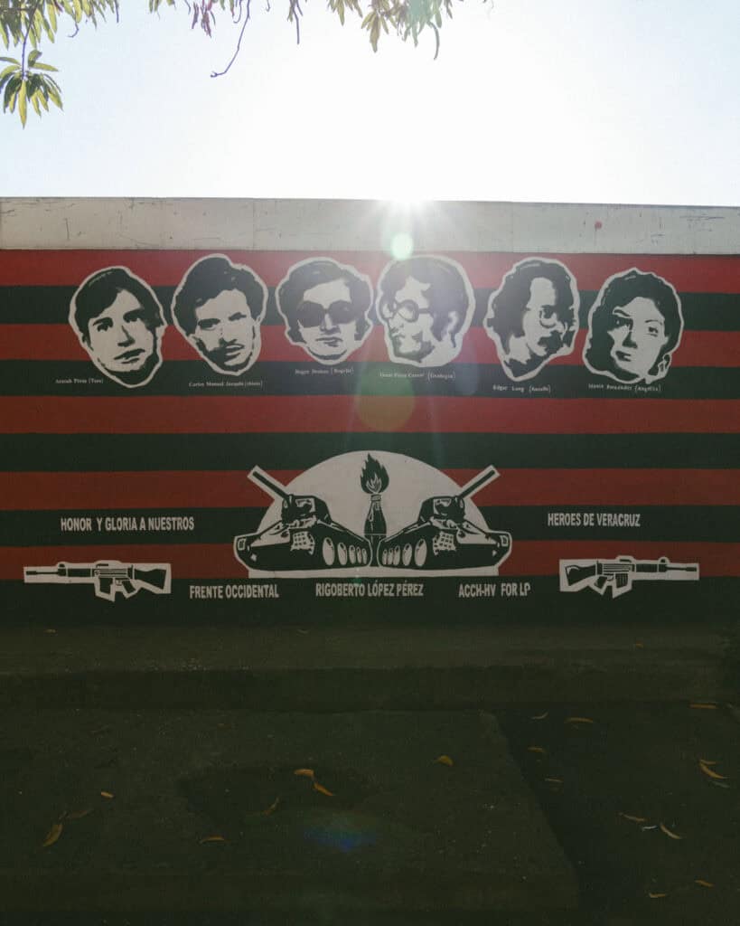 18 Best Things to Do in Leon, Nicaragua 15 A tribute mural with black and red stripes in the Revolution Museum, featuring portraits of six heroes labeled “Heroes de Veracruz” alongside illustrations of tanks and rifles.