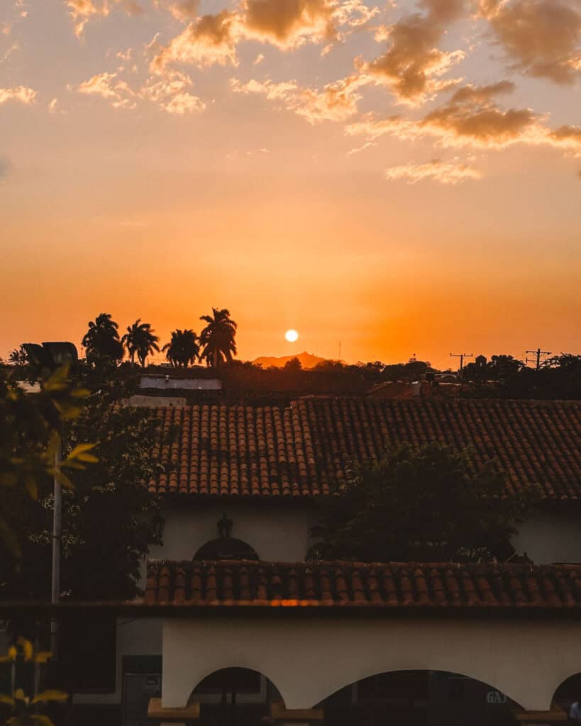 18 Best Things to Do in Leon, Nicaragua 34 A warm sunset over the red-tiled rooftops of León, Nicaragua, with silhouetted palm trees against a golden sky.