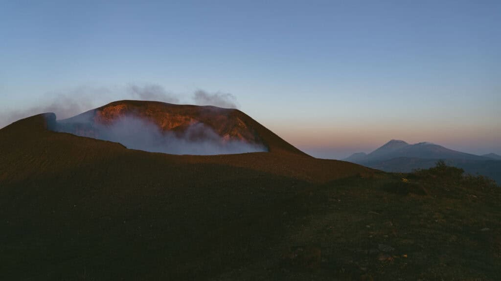Hiking Telica Volcano in Nicaragua: A Magical Sunrise 4 The smoldering crater of Telica Volcano at sunrise, emitting white smoke, with León’s volcanic range in the distance.