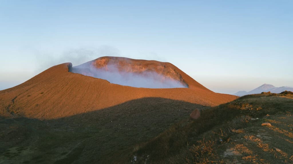 Hiking Telica Volcano in Nicaragua: A Magical Sunrise 12 A closer view of the Telica Volcano crater, surrounded by sunlit, reddish slopes and thin smoke clouds rising.