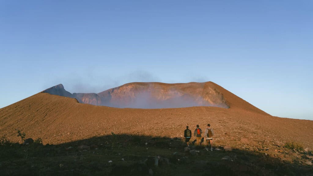 Hiking Telica Volcano in Nicaragua: A Magical Sunrise 8 Three hikers, including Brayden, approaching the expansive crater of Telica Volcano, with smoke wafting from the crater's depths.