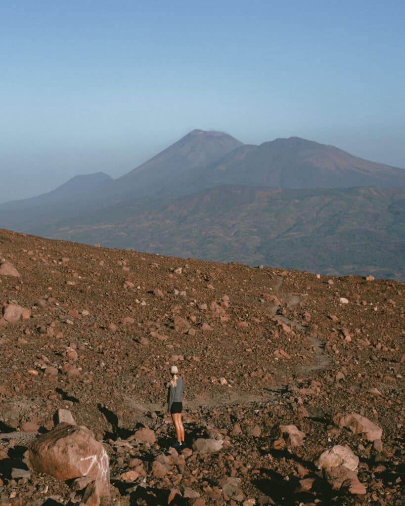 18 Best Things to Do in Leon, Nicaragua 3 Sally standing on a rocky terrain at Telica Volcano in León, Nicaragua, with distant volcanic peaks framed under a bright blue sky.
