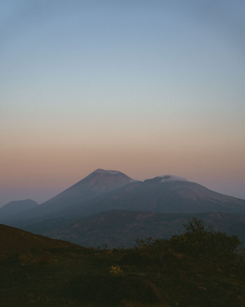 Hiking Telica Volcano in Nicaragua: A Magical Sunrise 6 Distant volcanic peaks slightly smoking in a soft, sunrise sky.
