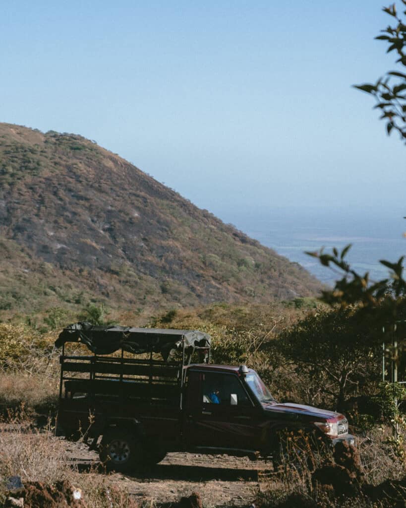 Hiking Telica Volcano in Nicaragua: A Magical Sunrise 17 A red pickup truck parked near the base of Telica Volcano, surrounded by lush vegetation and distant views of hills.