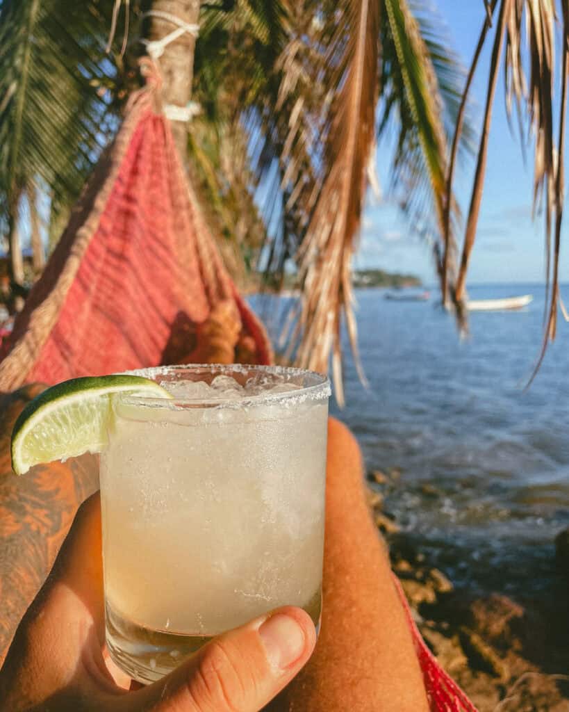 Corn Islands Nicaragua: Paradise on Big & Little Corn 42 A hand holding a margarita glass garnished with a lime, with a hammock and palm trees in the background at Desideri Café on Little Corn Island.