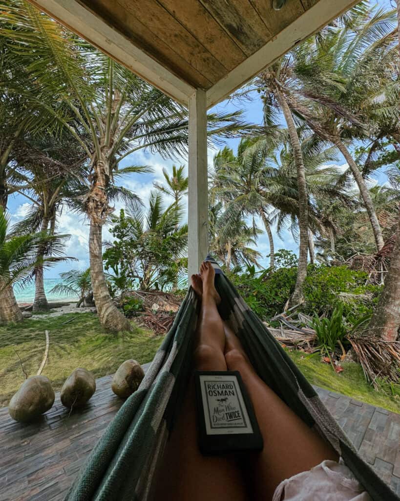 Corn Islands Nicaragua: Paradise on Big & Little Corn 39 A view from a hammock on Little Corn Island, with Sally's legs stretched out and an e-reader displaying "The Man Who Died Twice" by Richard Osman, framed by swaying palm trees.