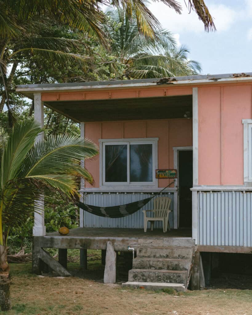 Nicaragua Travel Guide: Land of Lakes and Volcanoes 37 A pink bungalow labeled "Troy’s Place," surrounded by palm trees, with a hammock and chair on the porch. The tropical setting highlights the serene atmosphere of Little Corn Island.