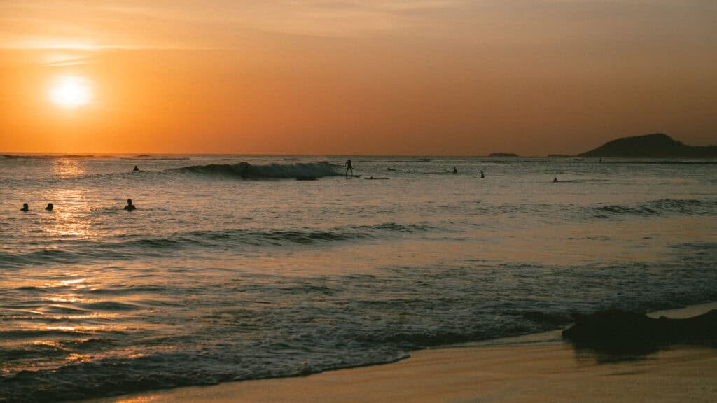 Popoyo, Nicaragua Travel Guide: Surf, Sand and Sunsets 11 Surfers catching waves in the glowing light of sunset at Popoyo Beach, with distant hills silhouetted against the sky.