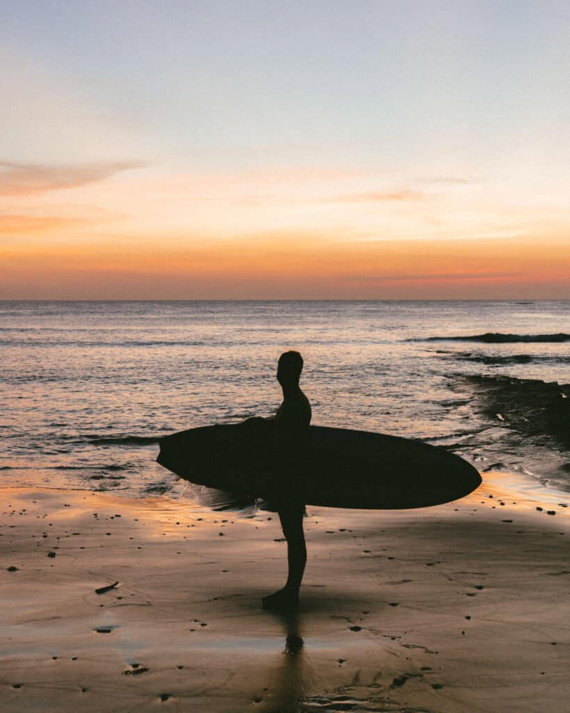 Popoyo, Nicaragua Travel Guide: Surf, Sand and Sunsets 16 Brayden silhouetted against the sunset on Popoyo Beach, with calm waves in the background and a surfboard in his arms.