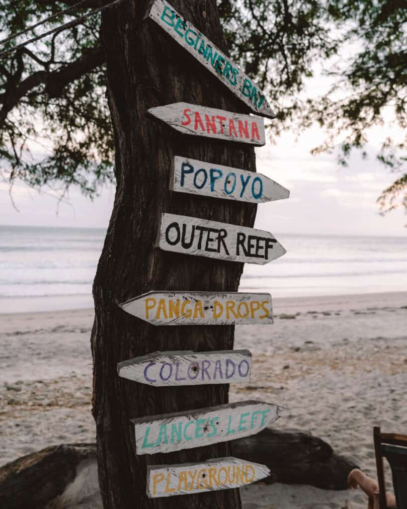 Popoyo, Nicaragua Travel Guide: Surf, Sand and Sunsets 15 Hand-painted wooden signs on a tree at Popoyo Beach, pointing to various surf spots like Beginners Bay, Santana, and Outer Reef.