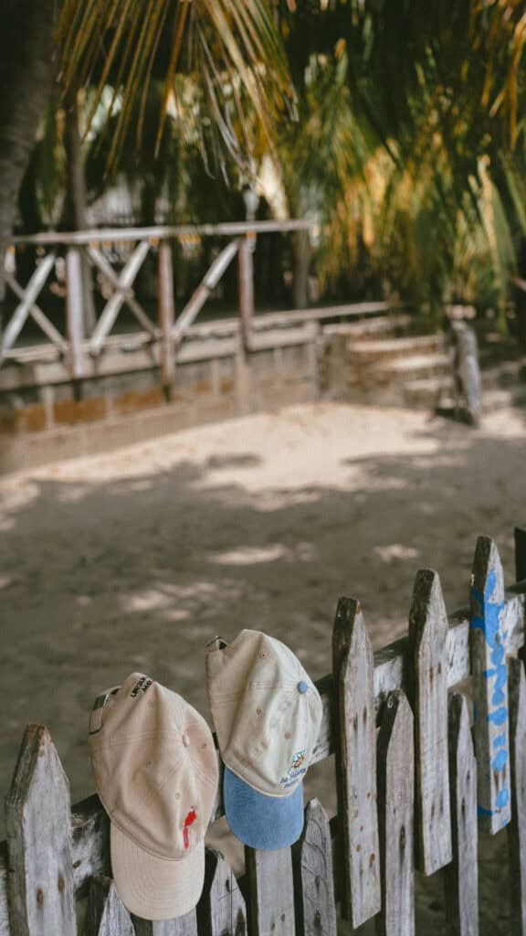 San Juan del Sur, Nicaragua Travel Guide: Worth the Hype? 31 Two worn caps hanging on a wooden fence near a sandy path lined with palm trees in San Juan del Sur, Nicaragua.