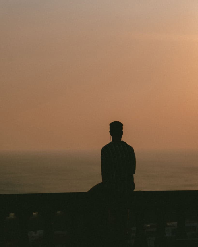 San Juan del Sur, Nicaragua Travel Guide: Worth the Hype? 1 A closer view of Brayden sitting on a railing at the Cristo de La Divina Misericordia viewpoint, framed by a vibrant sunset over the ocean.