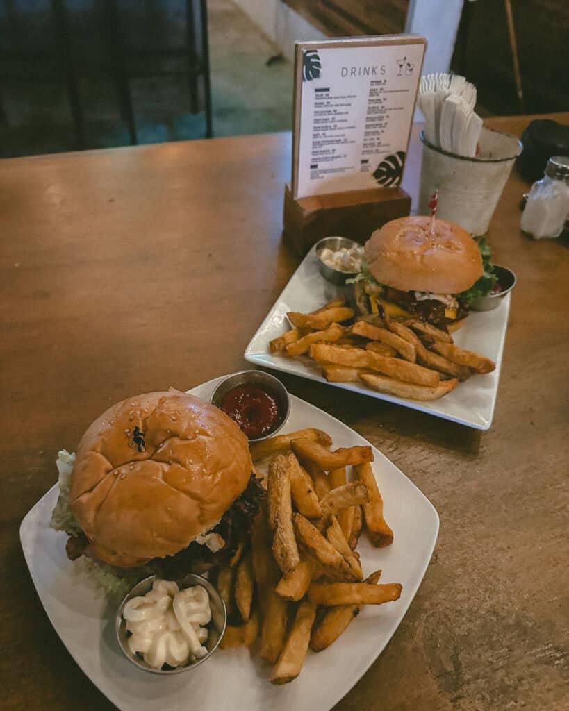 San Juan del Sur, Nicaragua Travel Guide: Worth the Hype? 40 Two plates of juicy burgers with crispy fries and condiments served on a wooden table at Dale Pues, accompanied by a drink menu in San Juan del Sur.