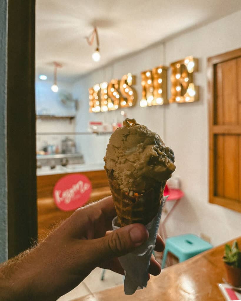 San Juan del Sur, Nicaragua Travel Guide: Worth the Hype? 41 A close-up of a hand holding an ice cream cone inside Kiss Me Ice Cream shop, with a glowing "Kiss Me" sign in the background in San Juan del Sur.