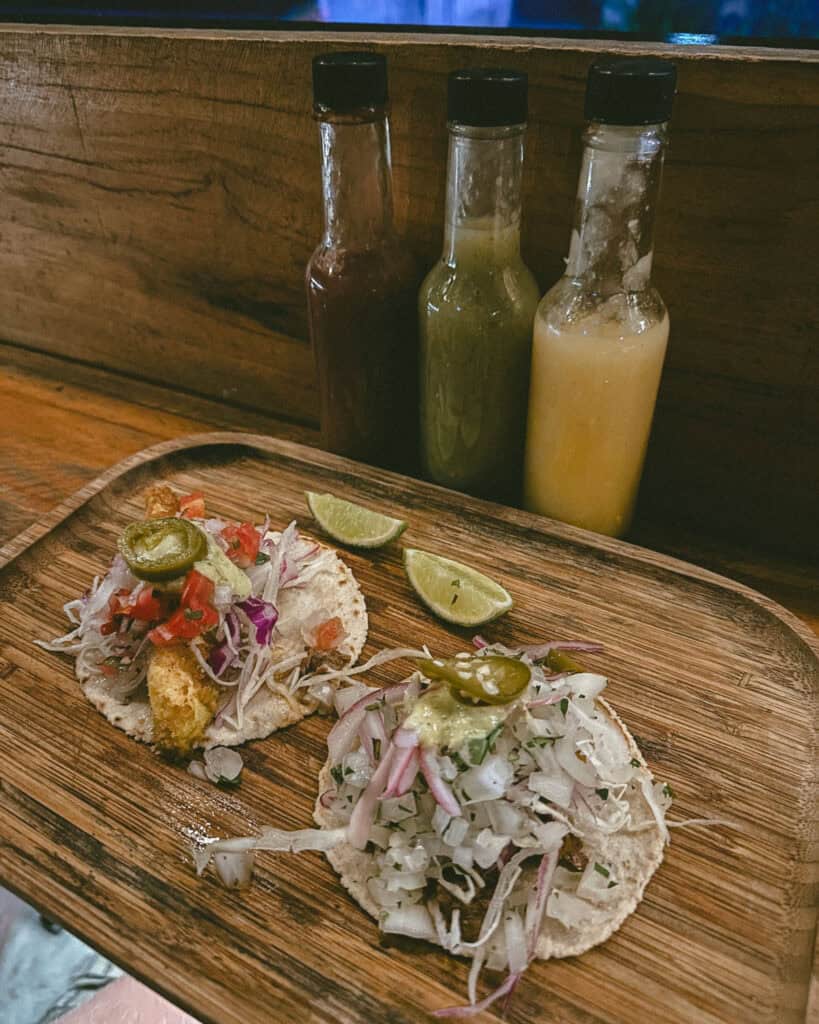 San Juan del Sur, Nicaragua Travel Guide: Worth the Hype? 38 A rustic table setting featuring tacos with vibrant toppings and lime wedges, accompanied by various hot sauces at Nacho in San Juan del Sur.