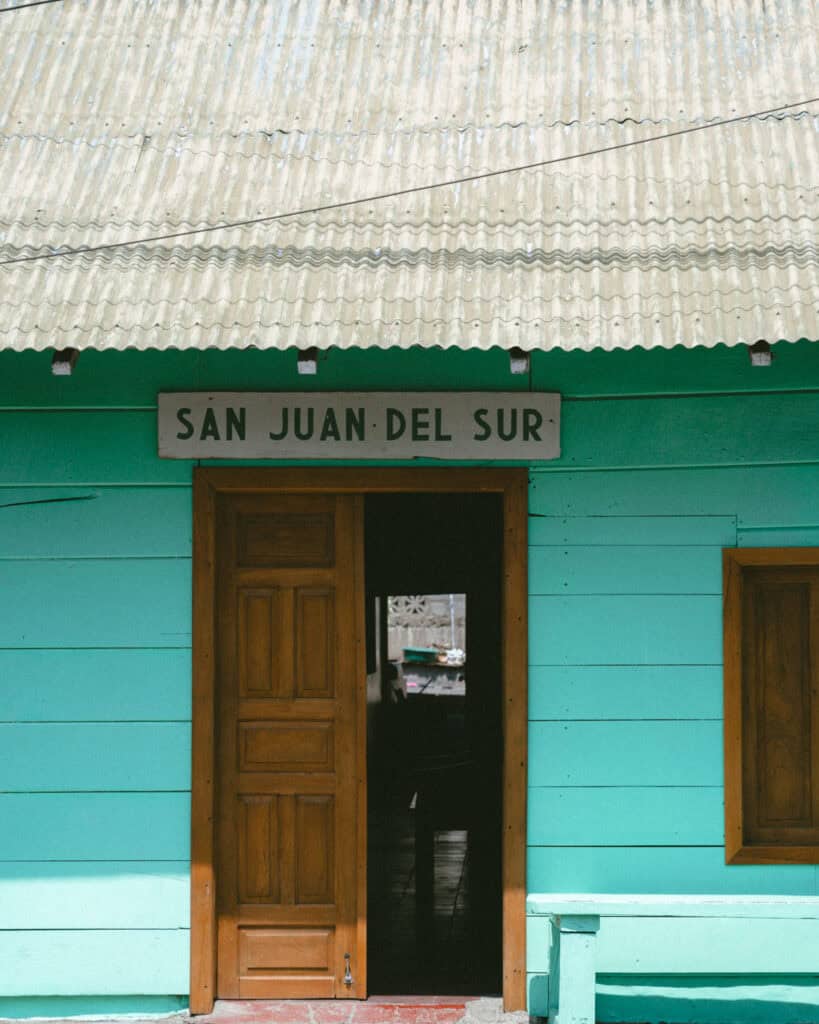 San Juan del Sur, Nicaragua Travel Guide: Worth the Hype? 3 A partially open wooden door on a turquoise wooden building with a sign 'San Juan del Sur' in block letters hung above the door.