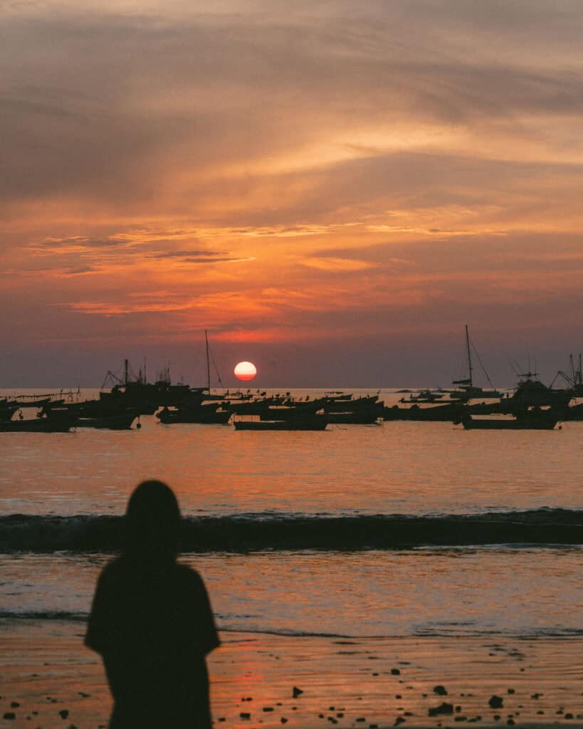 San Juan del Sur, Nicaragua Travel Guide: Worth the Hype? 27 Silhouette of Sally standing on the beach in San Juan del Sur, watching the vibrant sunset over the ocean, with boats anchored in the water.