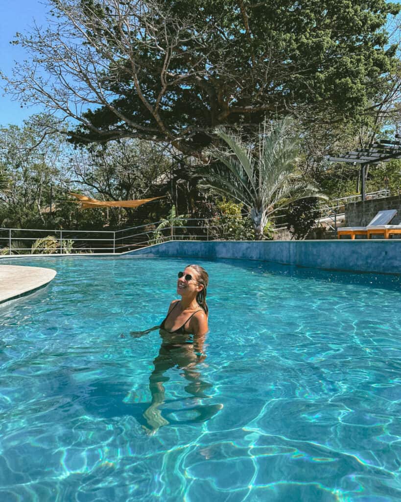 San Juan del Sur, Nicaragua Travel Guide: Worth the Hype? 22 Sally wading in the sparkling blue pool at TreeCasa Resort, smiling and enjoying the sunny weather amid a tropical backdrop.
