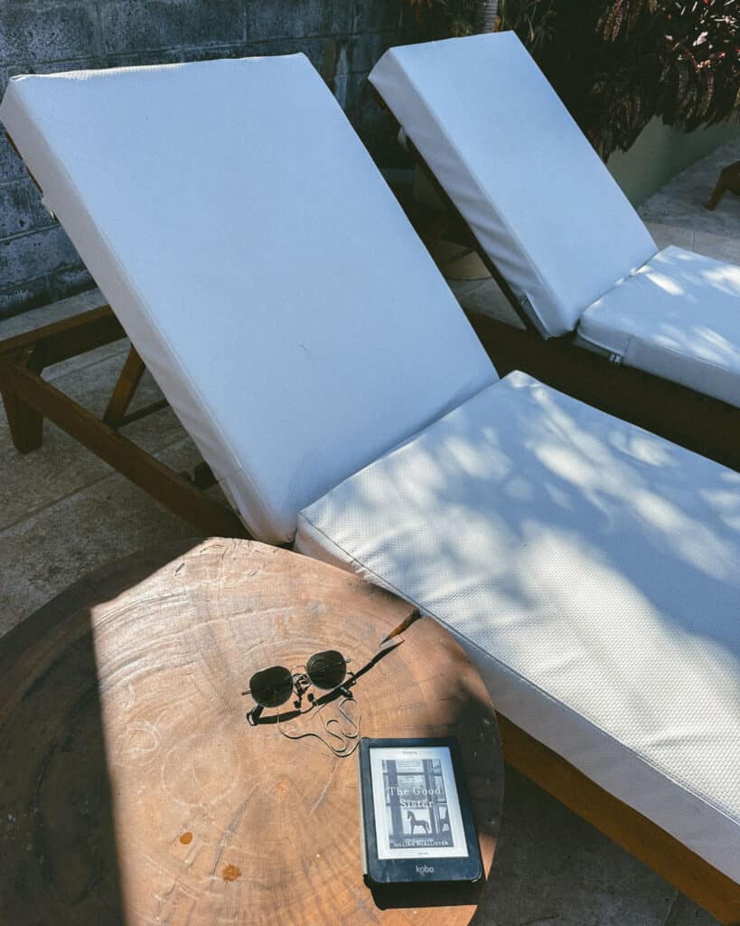San Juan del Sur, Nicaragua Travel Guide: Worth the Hype? 21 A serene poolside setup at TreeCasa Resort, featuring cushioned white sun loungers and a wooden side table holding sunglasses and e-reader.