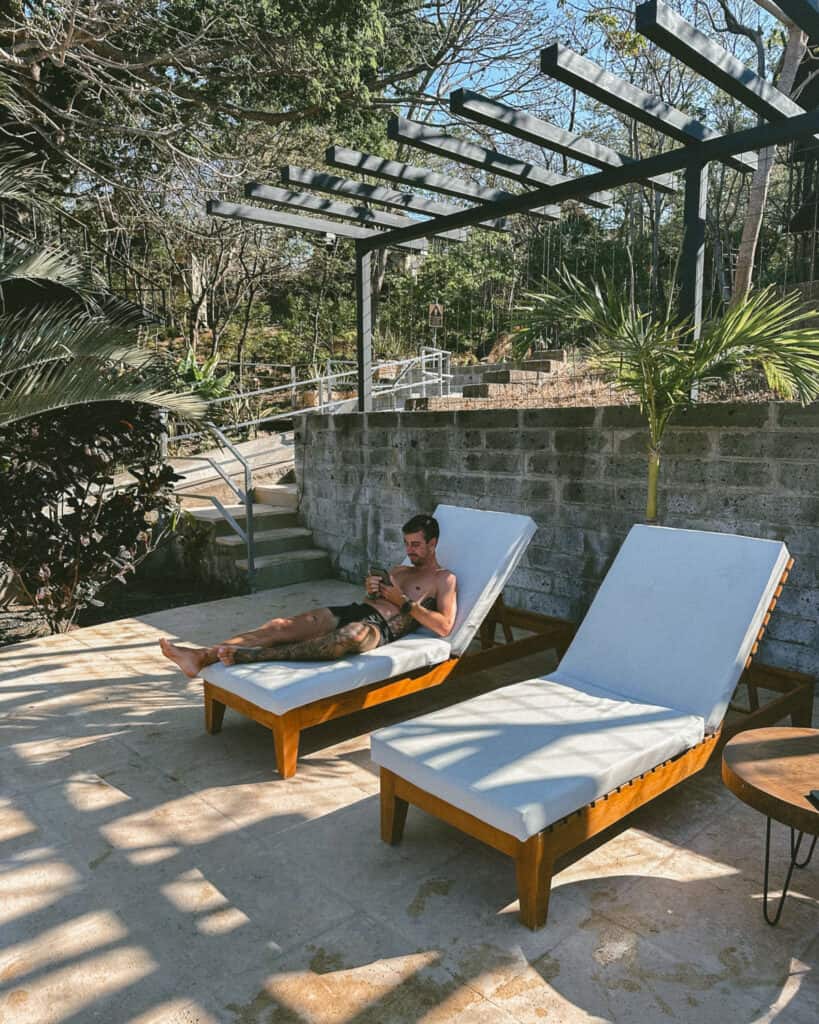 San Juan del Sur, Nicaragua Travel Guide: Worth the Hype? 23 Brayden relaxing on a sun lounger at TreeCasa Resort, shaded by pergolas and surrounded by lush plants and stone pathways.