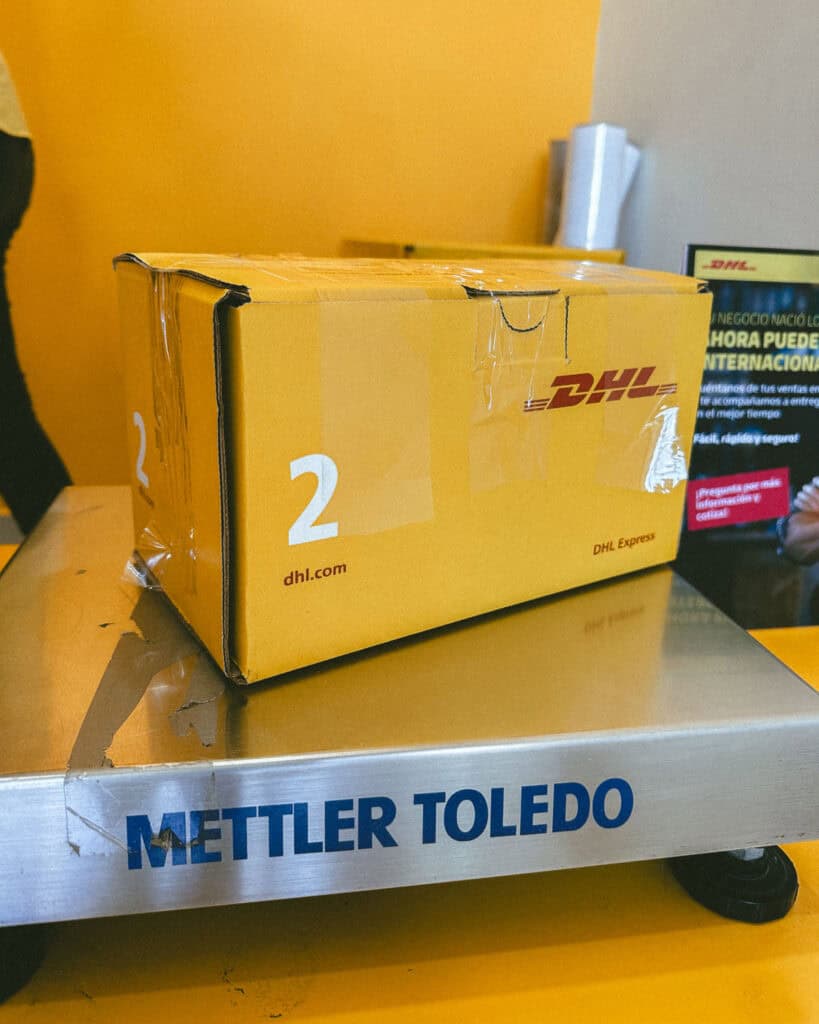 No Drones in Nicaragua: Our Solution 4 A yellow DHL cardboard box on a metal scale at a DHL store in El Salvador, sending a drone to Costa Rica as drones are not allowed in Nicaragua.